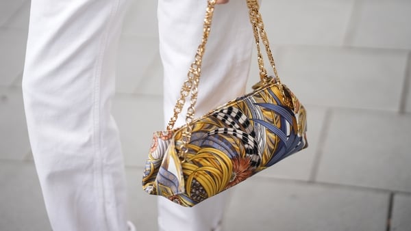 A colourful handbag held by a woman with white trousers