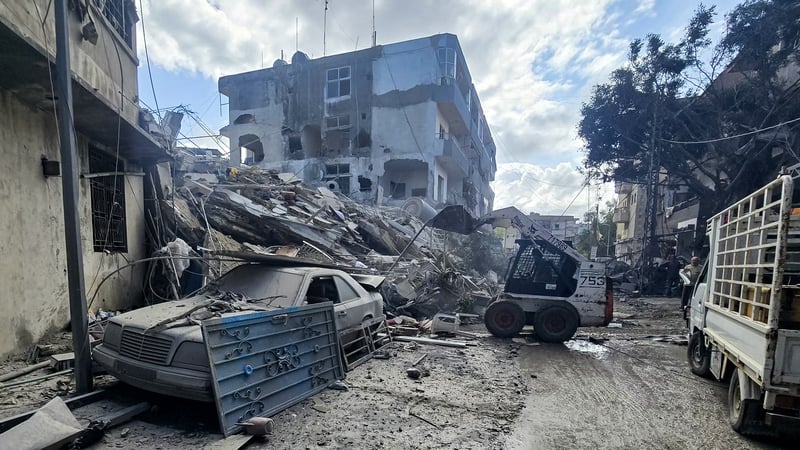 An excavator clears debris and rubble outside a damaged building