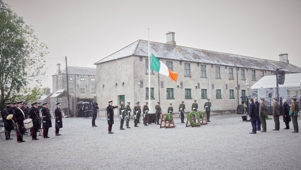 Members of the Irish Army stand near wreaths and a flag pole