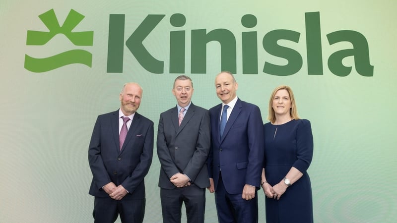 Three men and a woman pose for a photo with the Kinisla branding behind them on a green background