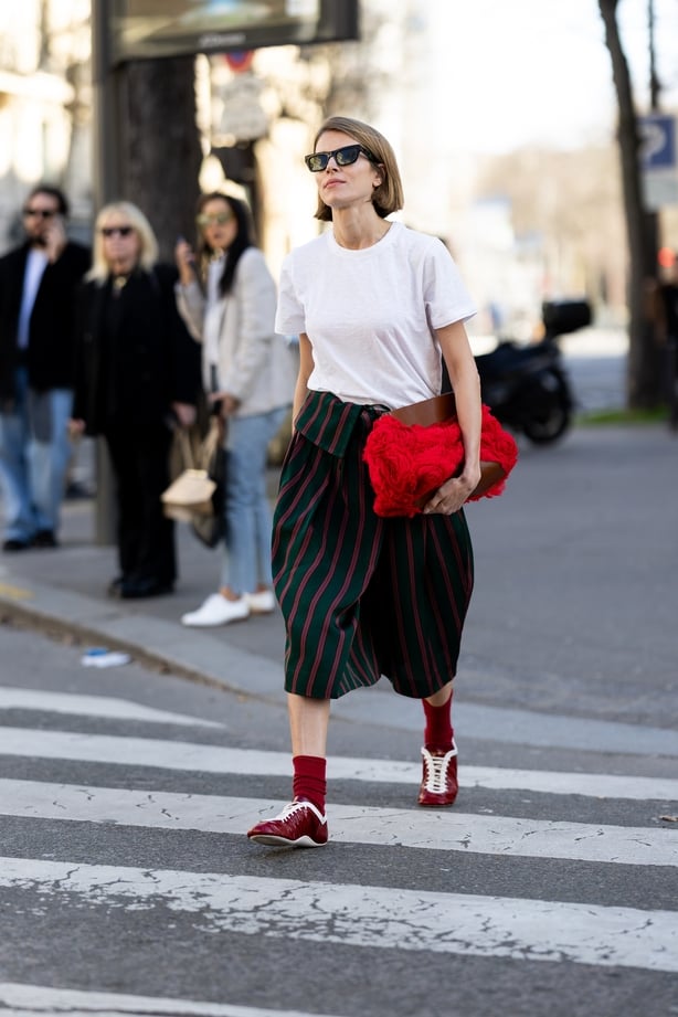 PARIS, FRANCE - MARCH 04: A guest wears red long socks, red sneakers, a green and pink striped high waist midi skirt, a red bag, a white t-shirt and black sunglasses outside Dries Van Noten show during Day Three of Paris Fashion Week - Womenswear Fall/Winter 2026/2027 on March 04, 2026 in Paris, Fra