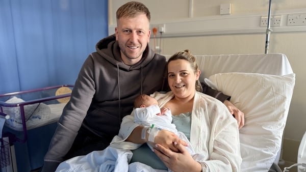 A man and woman hold a newborn baby in a hospital bed at Holles Street