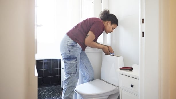Mid adult woman repairing cistern in bathroom during home renovation