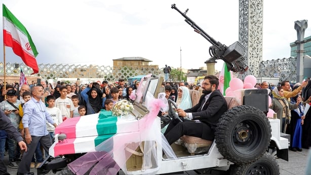 A bride and group couple rides in a military jeep arriving for a public mass wedding ceremony at Imam Hossein Square in Tehran on May 18, 2026. 