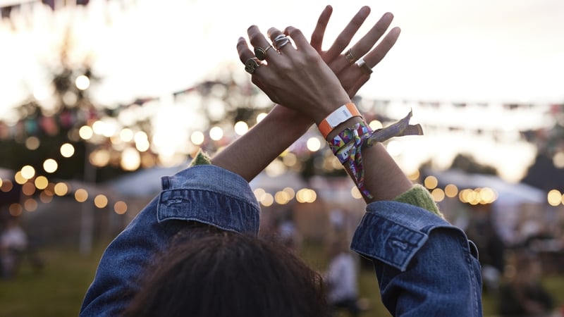 Woman with hands raised dancing at music festival during sunset