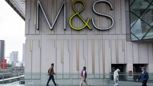 People walk by a big modern building with the M&S signage on it