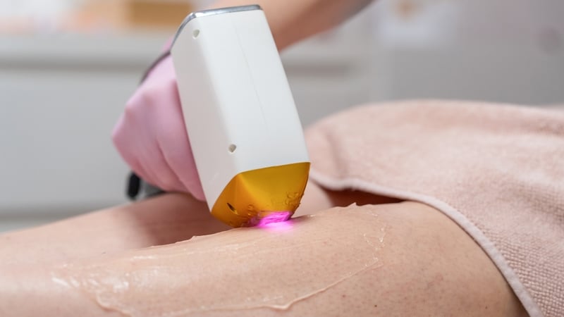 Close up image of a woman's legs while a beautician's hand holds a white laser hair removal device.