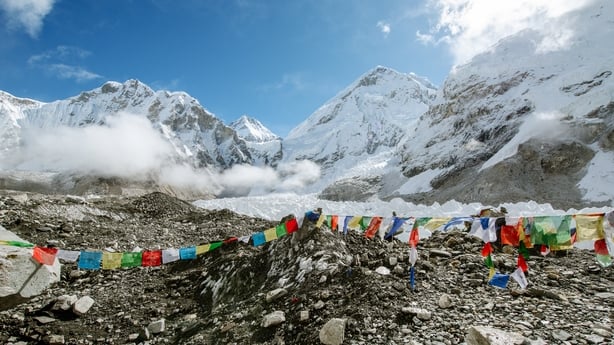 A string of brightly coloured flags hangs above rocks at Mount Everest Base Camp. The snowy mountain is visible in the background.