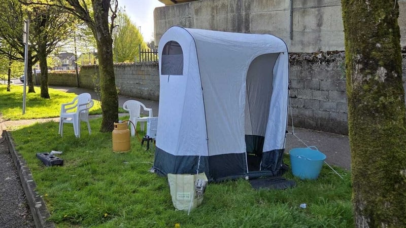Image shows a tall tent pitched on grass with some buckets beside it.