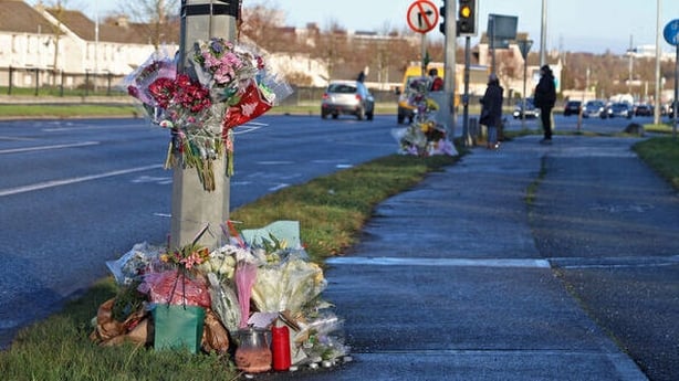 Floral tributes laid around a lamppost beside a road