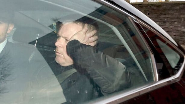 Man sits in car with hand on his head in image taken through rear window