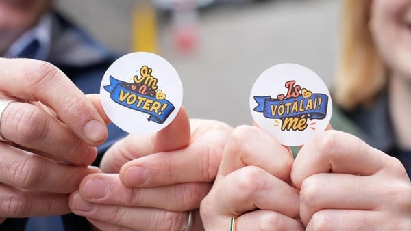 Two stickers being held up by a man and a woman. The sticker on the left says "I'm a voter" and the one on the right says "Is Vótalaí mé"
