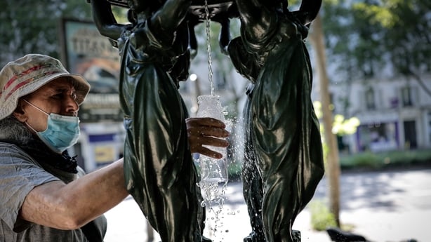 A man fills a glass of water at a public fountain in Paris