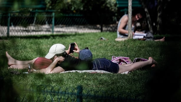 People lying down on grass reading and using their phone