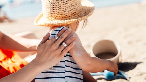 Mother putting sunscreen lotion on her child’s shoulders while sunbathing on the beach