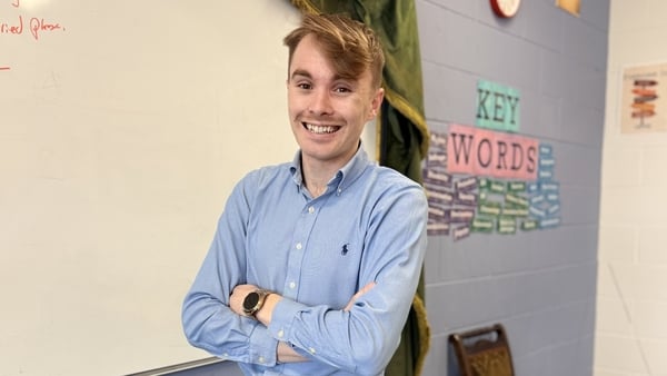 English teacher Thomas Dorian wears a blue shirt and stands with his arms folded in front of a whiteboard, looking at the camera and pictured from the waist up