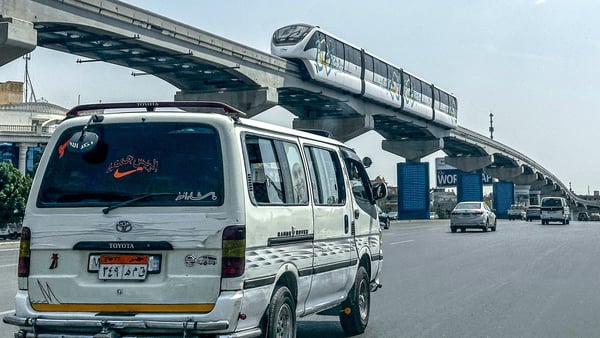 A minibus moves along a main road underneath new Cairo Monorail track as a train moves above