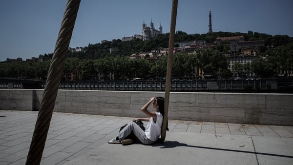 A woman sits on the dock of the Saone river in Lyon shielding her eyes from the sun
