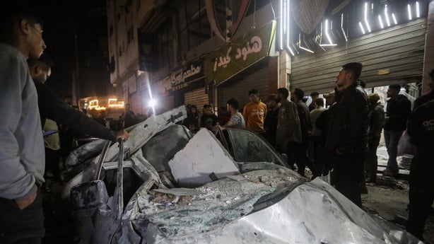 People stand around a destroyed car covered in debris