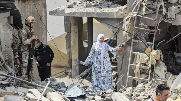 A woman makes her way through rubble as a Lebanese soldier looks on a