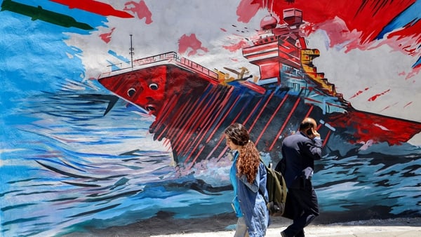 People walk past an anti-US and anti-Israel mural depicting missiles hitting an aircraft carrier in Tehran