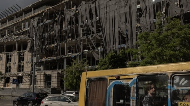 Comuters sit in a bus driving past a heavily damaged building following Russian strikes near the Lukianivska metro station in Kyiv