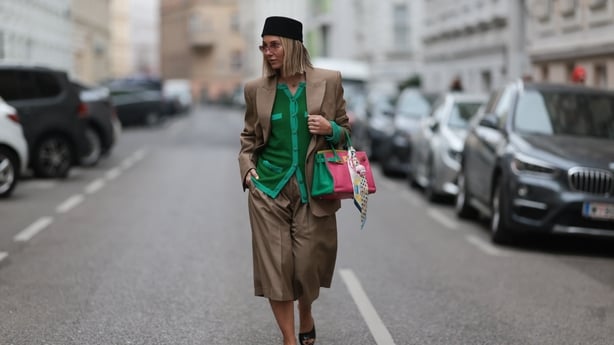 VIENNA, AUSTRIA - MARCH 16: Karin Teigl is seen wearing a bright green Chanel cardigan with a V-neck and matching buttons, a taupe H&M Studio blazer with a relaxed fit, and matching wide-legged culottes. She also wears black Alaia patent leather wedge mules, a black brimless Nakd hat, rimless pink-t