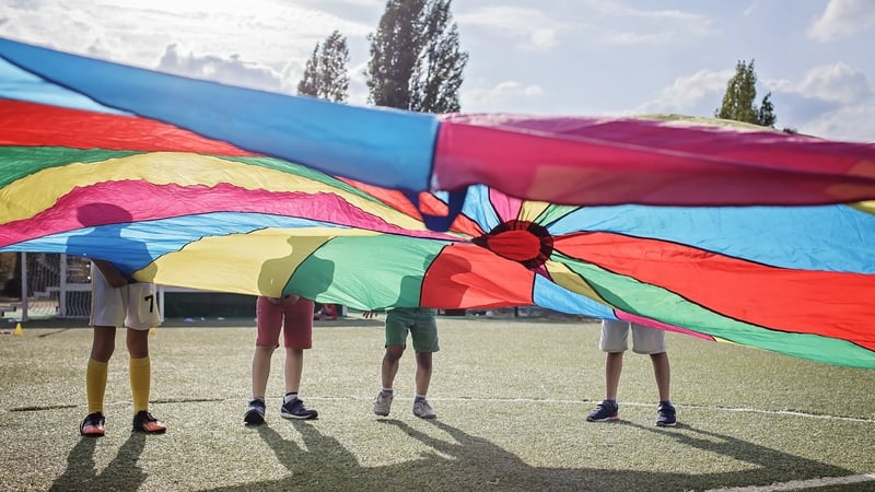Group of friends playing and waving bright colorful parachute, outdoors party, summer school camp