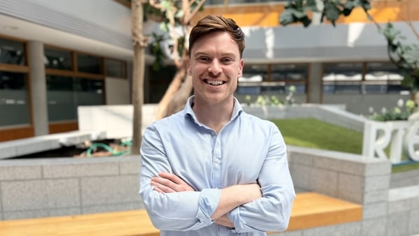 TJ Hegarty stands with his arms crossed looking at the camera, he is photographed from the waist up and is smiling