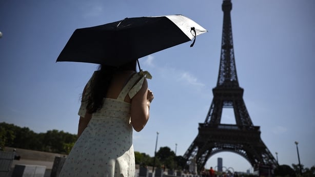 A woman uses an umbrella to protect herself from the sun near the Eiffel Tower in Paris