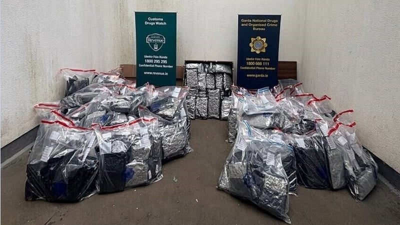 Dozens of packages of cannabis in evidence bags placed in a room in front of An Garda Síochána and Revenue signs