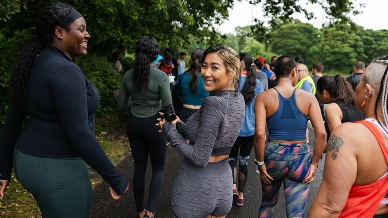 An over the shoulder view of a large group of people who are taking part in an inclusive race which is open to all ages and abilities and even open to dogs. They are all walking toward the starting line after doing some warm up exercises in a group.