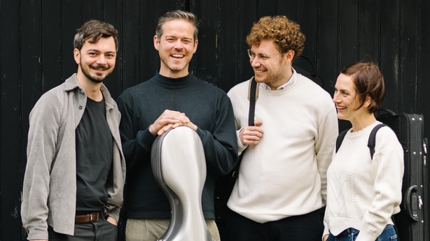Four members of the Gealán Quartet stand in a row. They are smiling and laughing at each other.