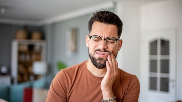 Young man suffering from a strong toothache, touching his cheek at home