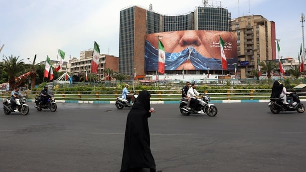 An Iranian woman crosses the road next to a political billboard featuring US President Donald Trump and the Strait of Hormuz erected on a building in Valiasr Square, in Tehran on May 28, 2026. Iran's foreign ministry condemned on May 28, what it called violations by the United States after its strik