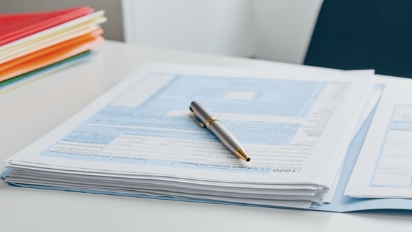 A close-up view of stacked tax forms with a pen placed on top