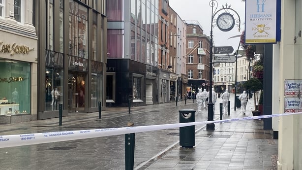 A number of people in white forensic suits on a street with garda crime tape in the foreground