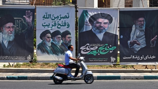 A man rides a scooter past installed banners with pictures of Iran's slain supreme leader Ayatollah Ali Khamenei