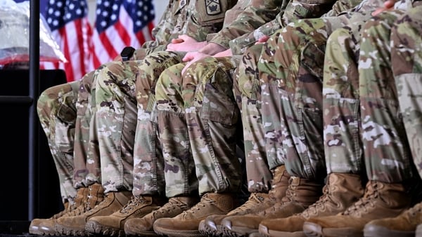 a row of soldiers in uniform sitting down with an american flag to the side