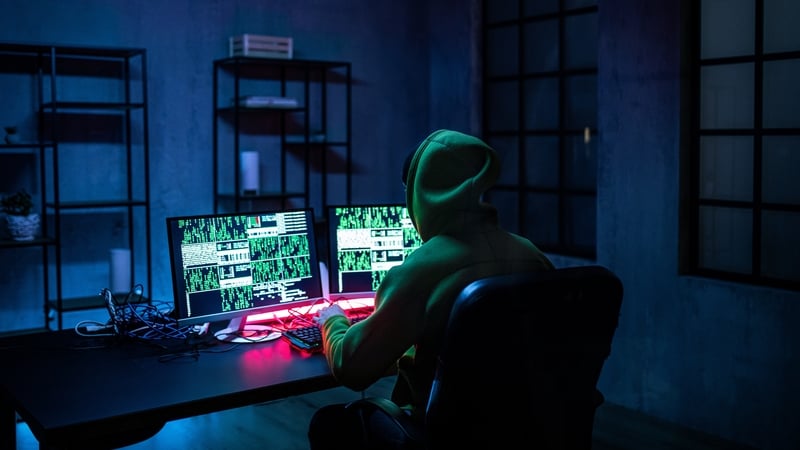 Hacker man working on computers alone in dark room, rear view.