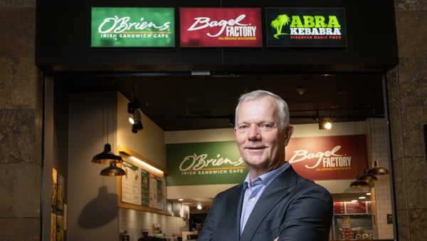Image of a business man standing in front of the branding of quick service restaurant brands O'Briens, Bagel Factory and Abrakebabra