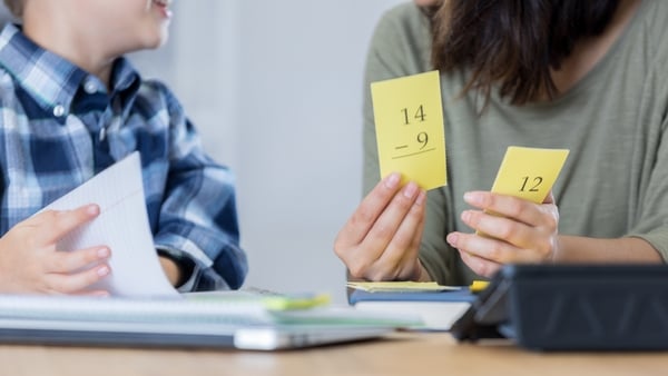 Woman holds subtraction flashcards beside a schoolboy