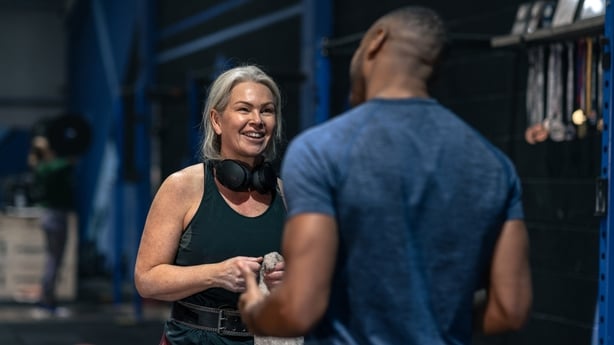 A personal trainer and a mature woman sharing encouragement at a gym. 